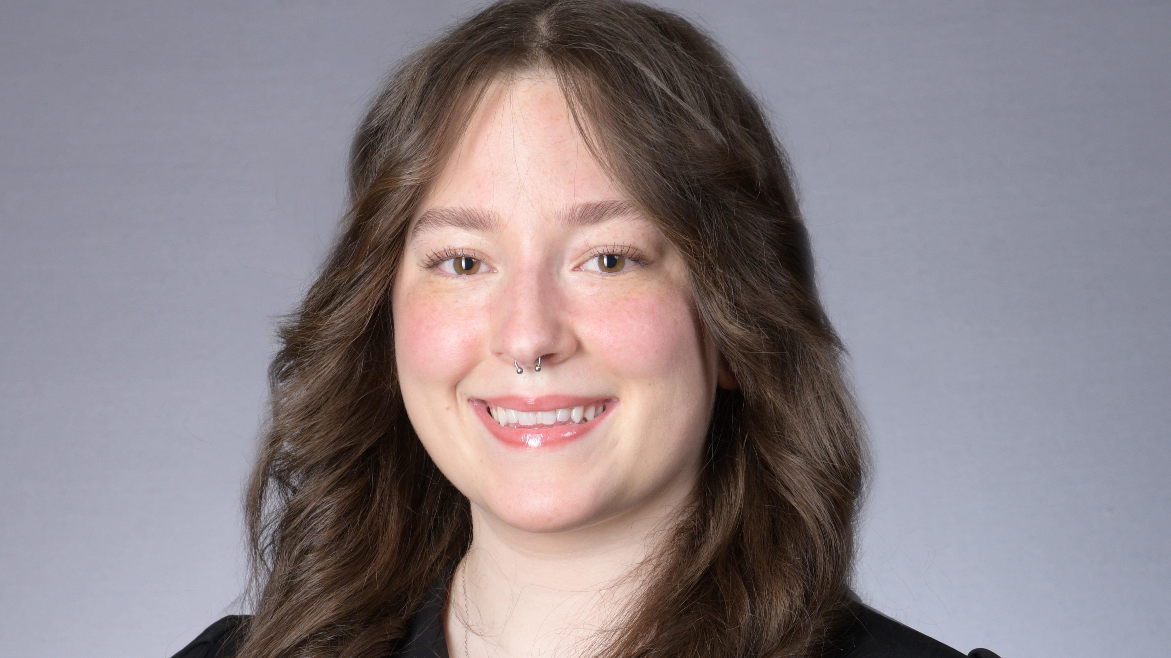 Olivia Kiefer smiles in front of a gray background in a black blazer over a white shirt.